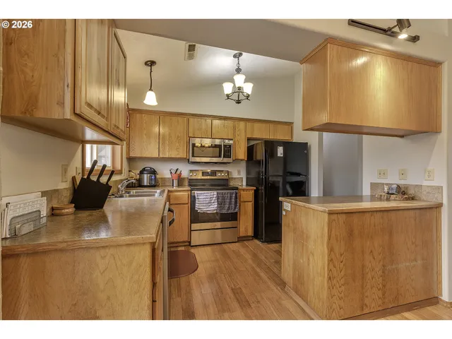 a kitchen with stainless steel appliances kitchen island granite countertop a refrigerator a stove top oven and a sink with wooden floor