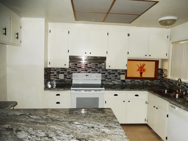 a large kitchen with granite countertop a stove a sink and white cabinets
