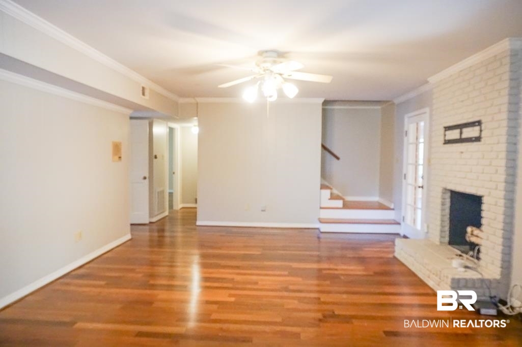 255 Suffolk Road Mobile, AL 36608 - Photo 14 of 29 Unfurnished living room featuring wood finished floors, crown molding, a ceiling fan, and a brick fireplace