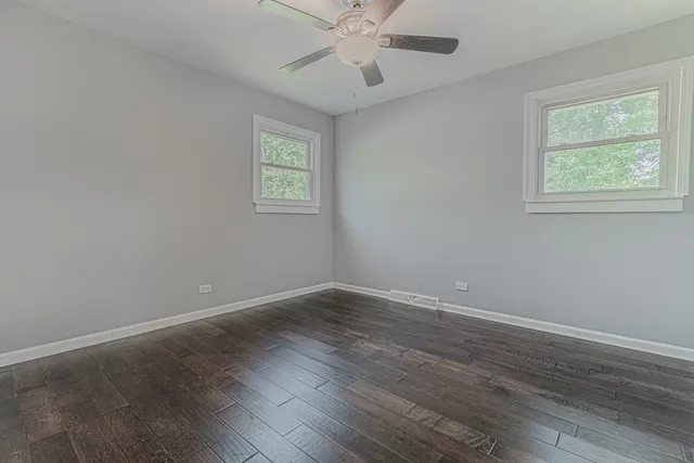 an empty room with wooden floor chandelier fan and windows