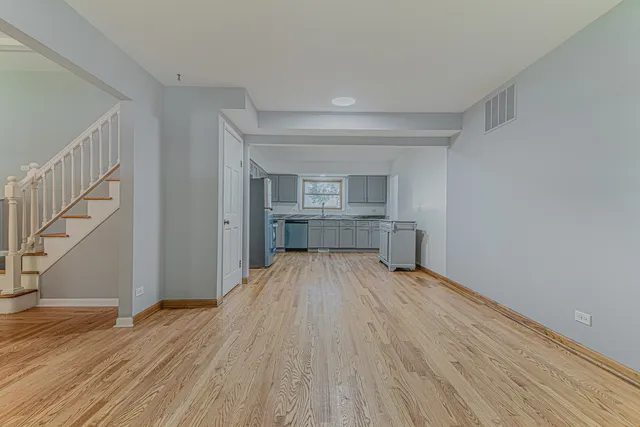 a view of empty room with wooden floor and kitchen