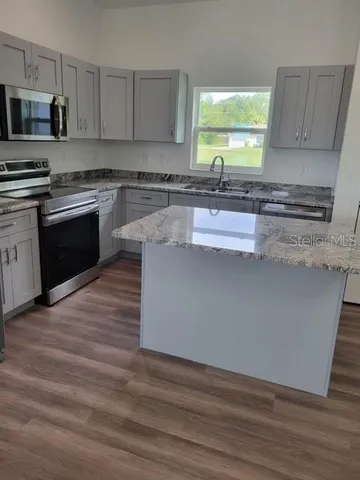 a kitchen with granite countertop wooden floors appliances a sink and a window