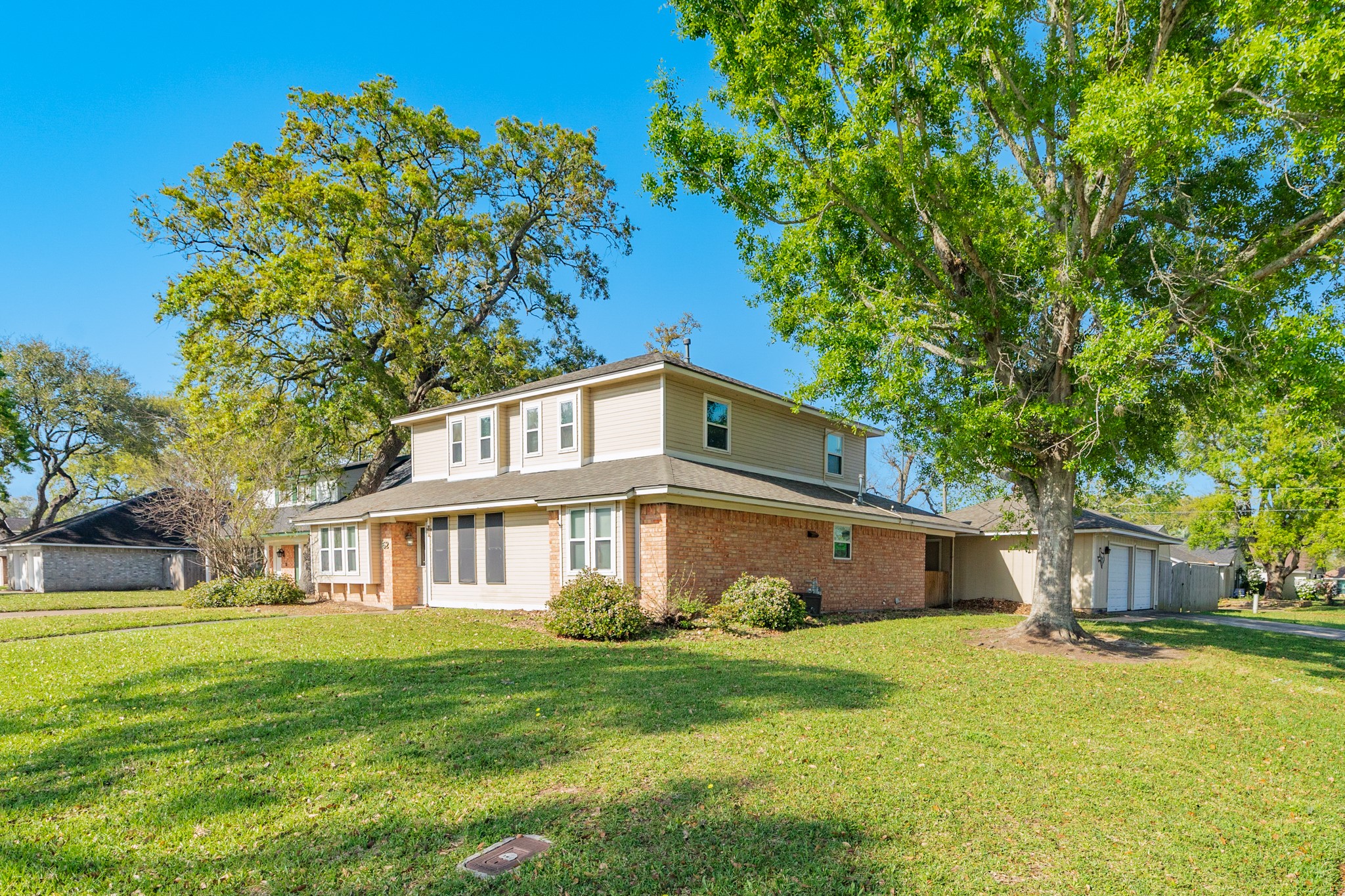 Charming two-story home with a brick and siding exterior, set on a spacious, well-maintained lawn. Mature trees provide shade and curb appeal. The house features a detached garage and is located in a serene neighborhood.
