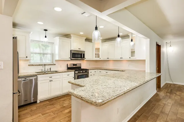 a kitchen with granite countertop a stove a sink a center island and wooden floor