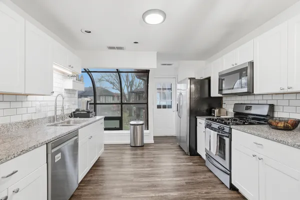 a kitchen with stainless steel appliances a stove top oven a sink a refrigerator white cabinets and wooden floor