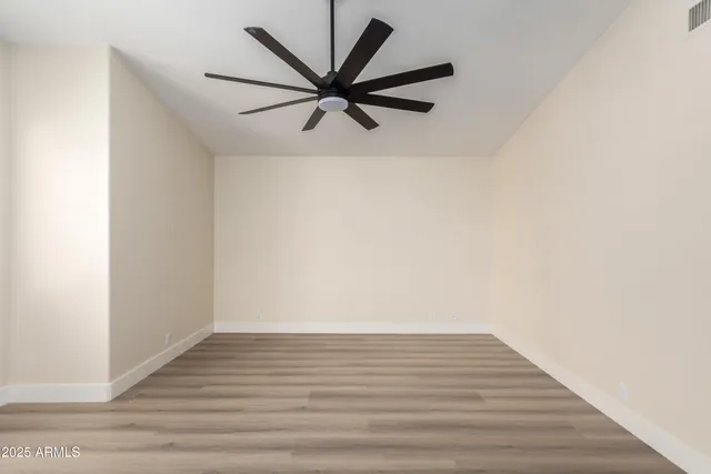 an empty room with wooden floor chandelier fan and windows