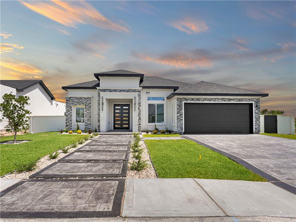 Prairie-style home with stone siding, roof with shingles, french doors, a garage, and a yard
