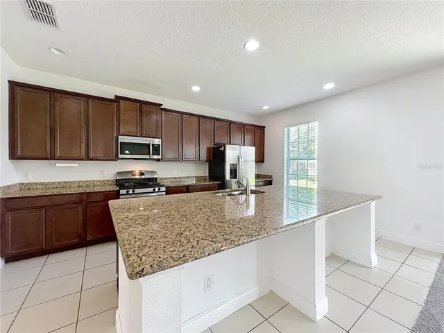 a kitchen with granite countertop stainless steel appliances a sink dishwasher a stove top oven a refrigerator with wooden cabinets and floor