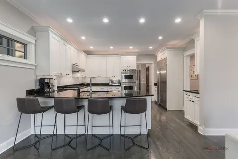 a kitchen with stainless steel appliances kitchen island granite countertop a refrigerator a stove a sink counter and chairs