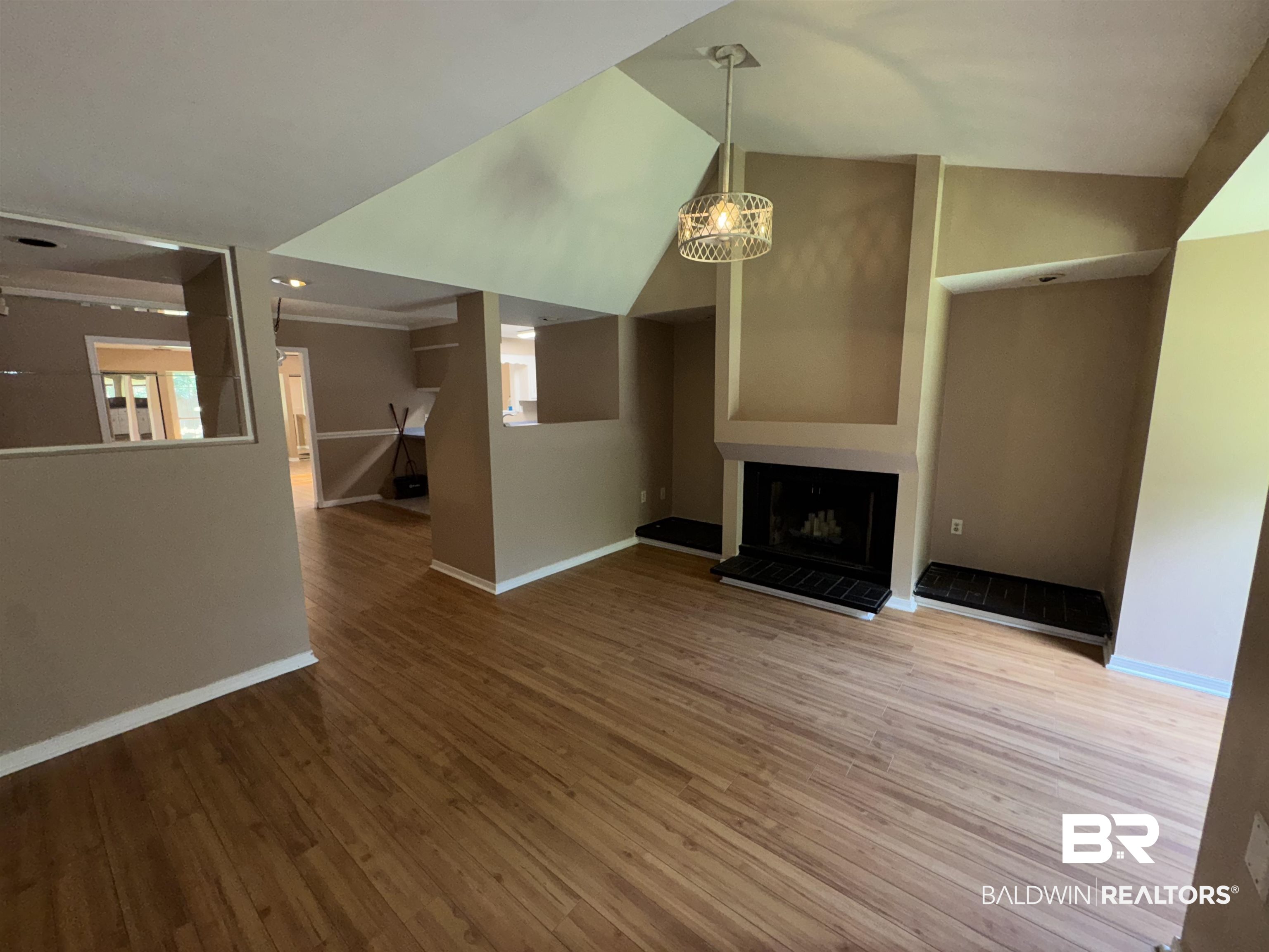 8070 Middle Ring Road Mobile, AL 36619 - Photo 8 of 26 Unfurnished living room featuring wood finished floors, a chandelier, a fireplace with raised hearth, and high vaulted ceiling