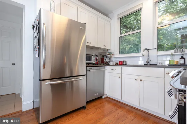 a kitchen with white cabinets white stainless steel appliances and window