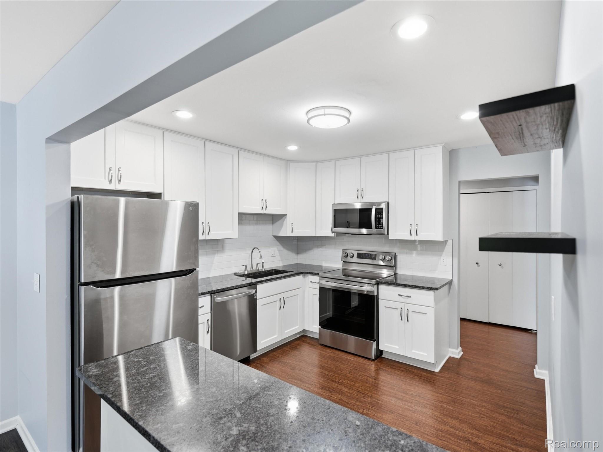 29636 Middlebelt Road, Unit 2602 Farmington, MI 48334 - Photo 13 of 34 Modern kitchen featuring white shaker cabinetry, stainless steel appliances, speckled stone countertops, a subway tile backsplash, and wood-finish flooring