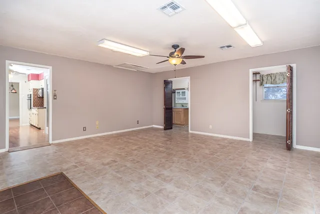 an empty room with chandelier fan and windows