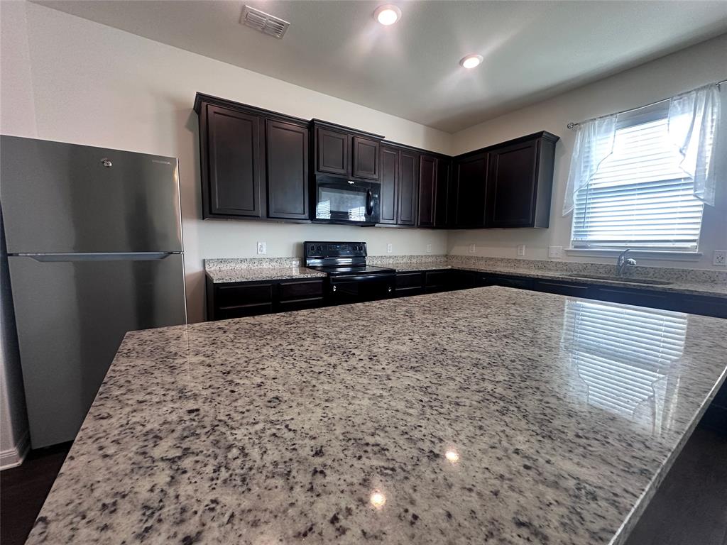 14310 Wrangler Way Dallas, TX 75253 - Photo 8 of 29 a kitchen with kitchen island a refrigerator sink and wooden cabinets