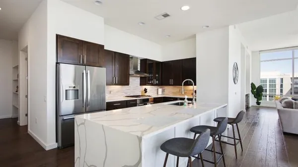 a kitchen with stainless steel appliances a refrigerator a stove a sink a dining table and chairs with wooden floor