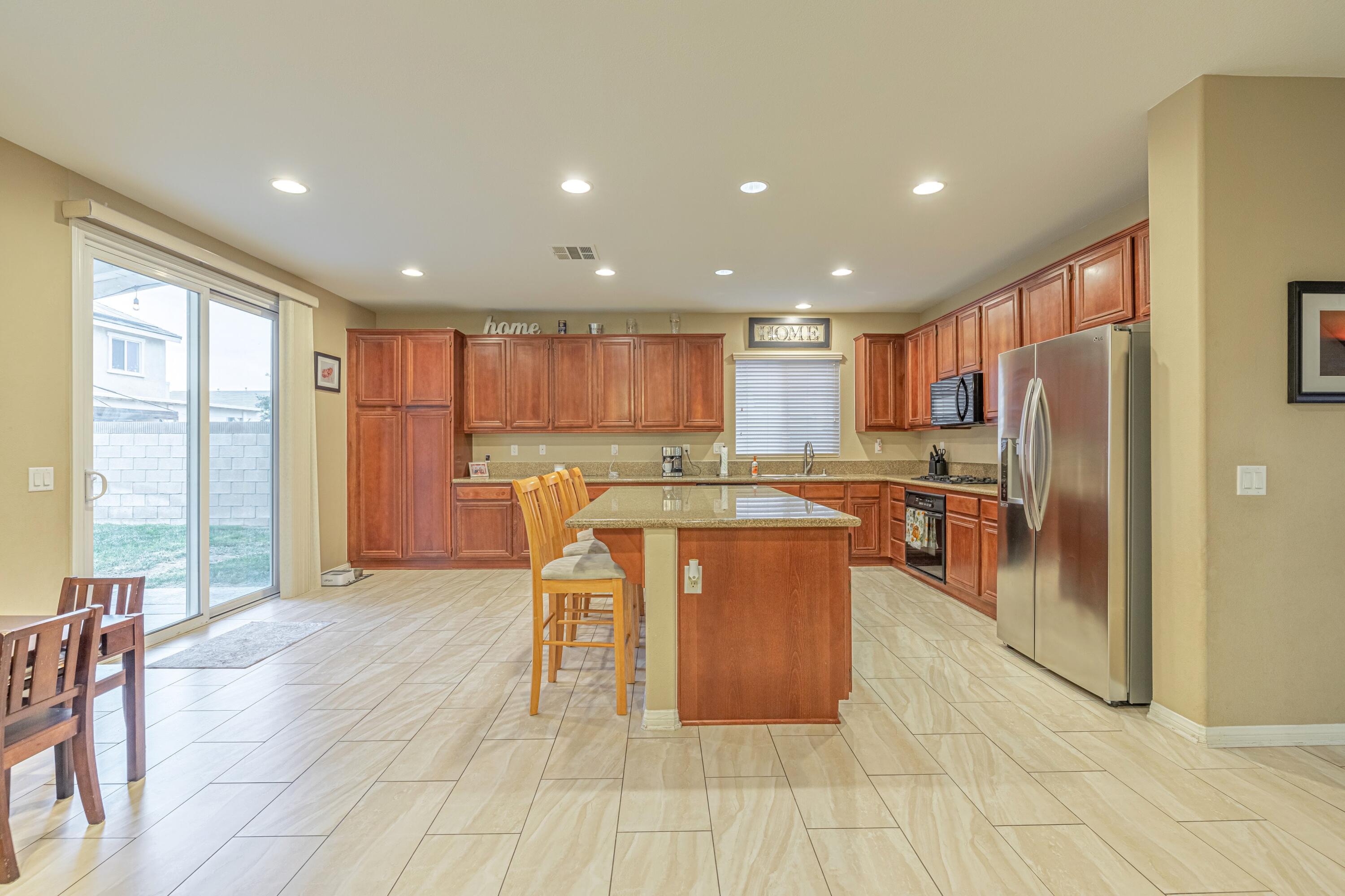 4403 Edam Street Lancaster, CA 93536 - Photo 16 of 42 a kitchen with stainless steel appliances granite countertop a refrigerator a stove top oven and a dining table with wooden floor