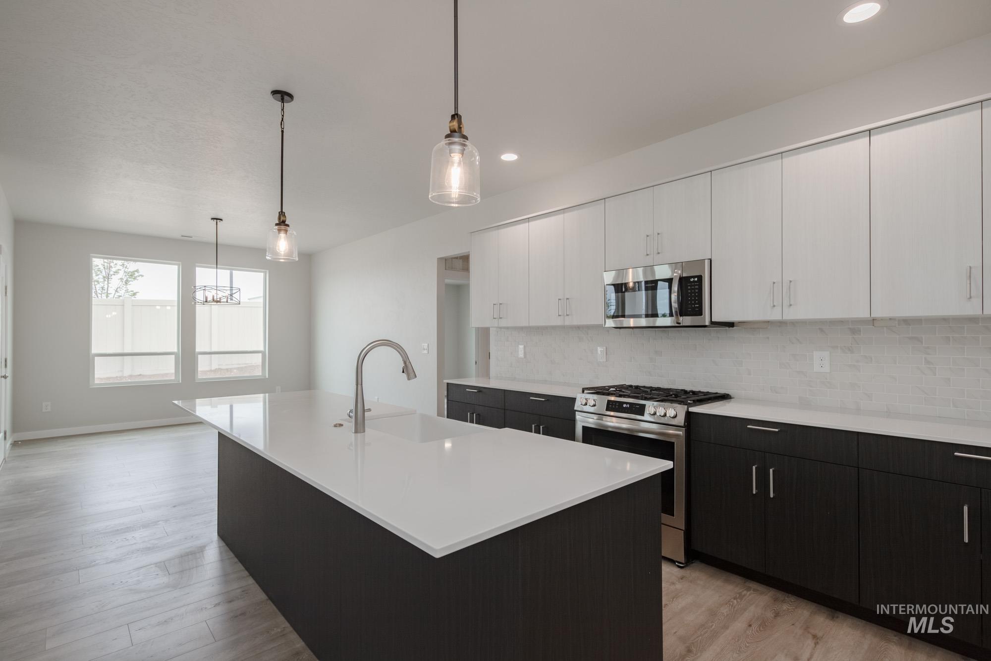 5261 South Memory Avenue Meridian, ID 83642 - Photo 4 of 30 Two tone kitchen with two tone color scheme, stainless steel appliances, hanging light fixtures, a center island with sink, and light wood finished floors
