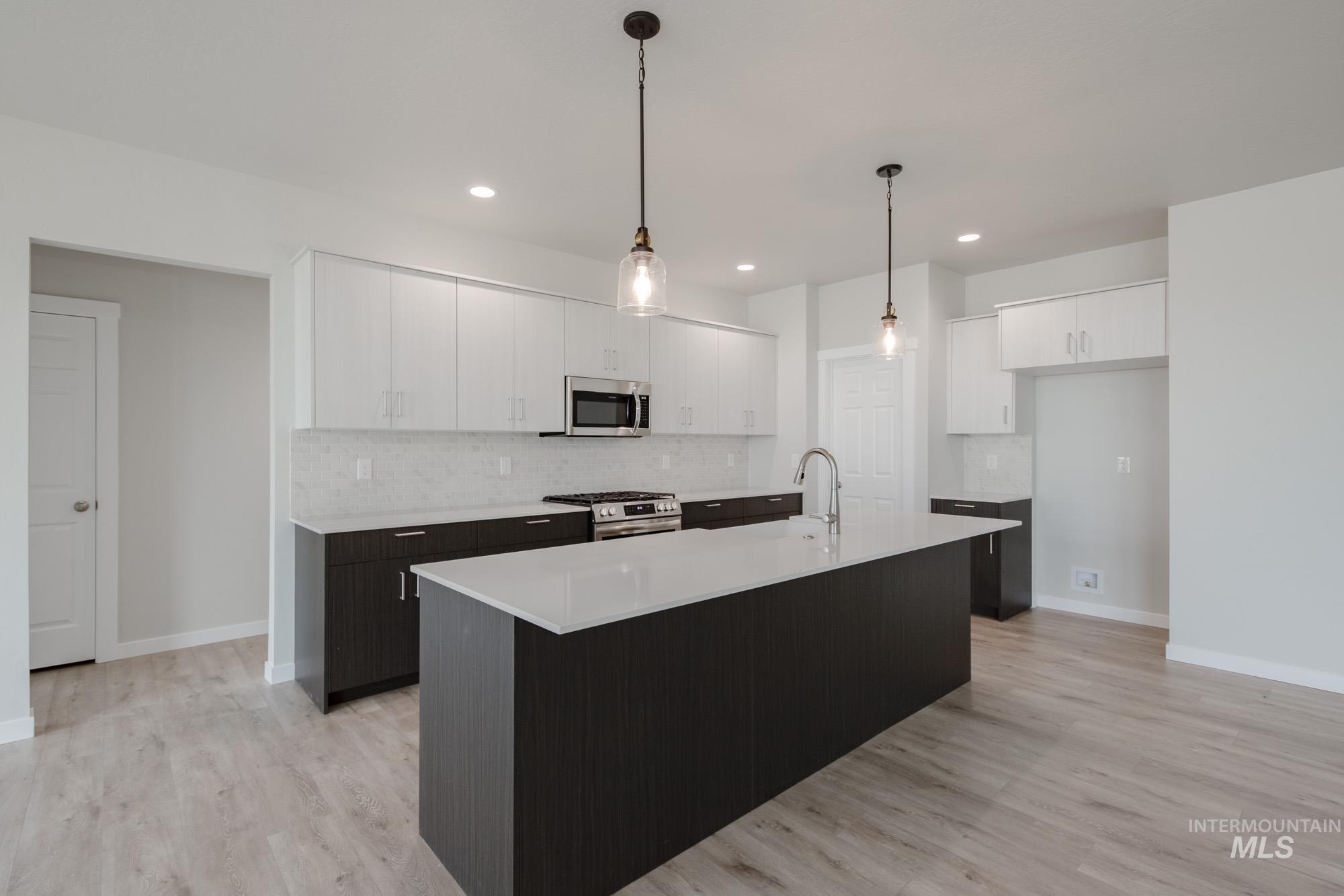 5261 South Memory Avenue Meridian, ID 83642 - Photo 6 of 30 Kitchen with two tone color scheme, hanging light fixtures, stainless steel appliances, an island with sink, and light wood-style floors