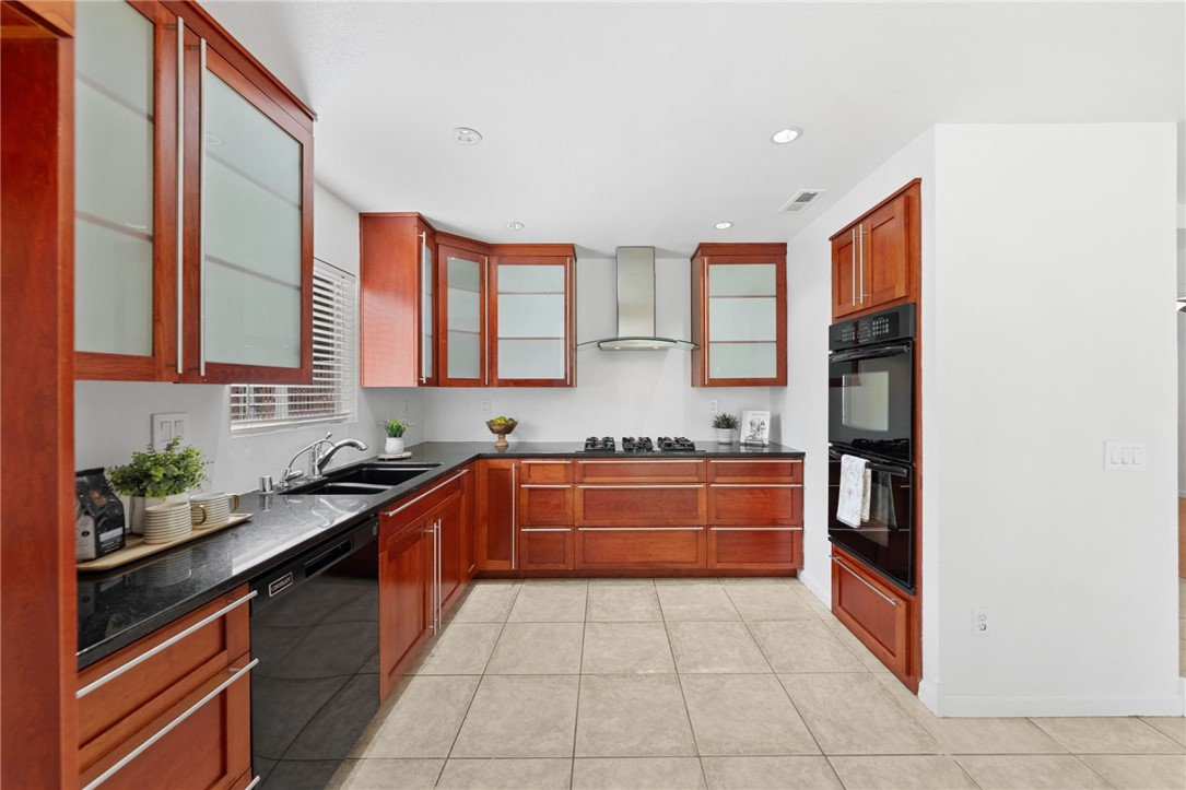 6090 Meadowbrook Lane Riverside, CA 92504 - Photo 12 of 37 Updated cabinetry with frosted-glass uppers, dark countertops, and a sleek vent hood over the cooktop.