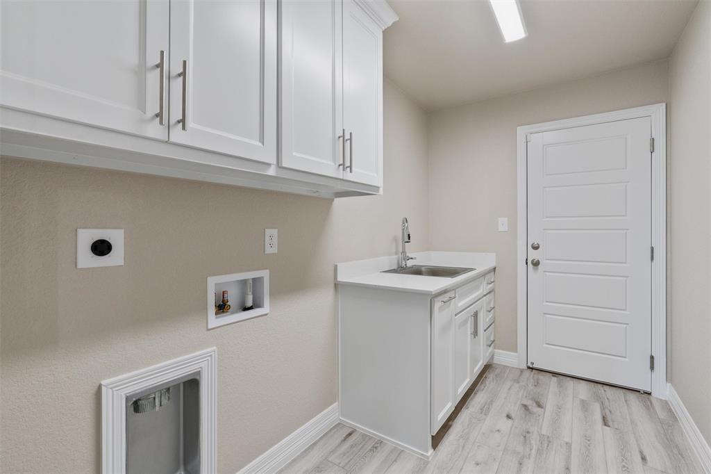 1341 Promised Land Road Hewitt, TX 76643 - Photo 21 of 29 Laundry room featuring white cabinetry, a utility sink with a stone-finish countertop, light wood-finish flooring, and a modern paneled door