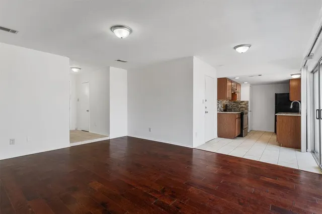 a view of an empty room with wooden floor and a kitchen