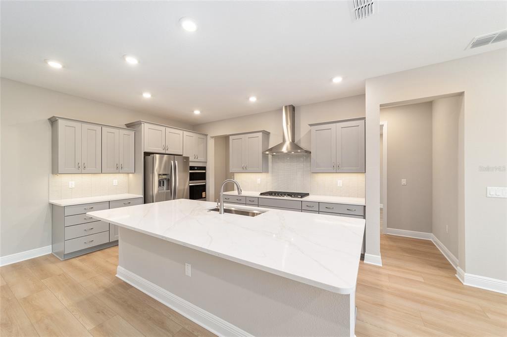 10305 Southwest 105th Street Ocala, FL 34481 - Photo 19 of 44 a large kitchen with stainless steel appliances kitchen island a stove a refrigerator a oven and white cabinets with wooden floor