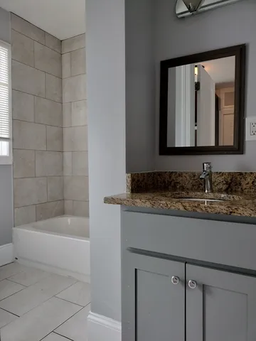 a bathroom with a granite countertop sink a mirror and a bathtub
