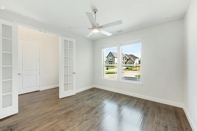 an empty room with wooden floor chandelier fan and windows