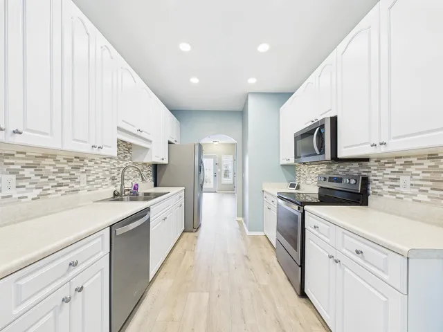 a kitchen with a sink dishwasher a white stove refrigerator and white cabinets with wooden floor