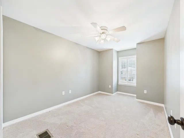 an empty room with a chandelier fan and windows