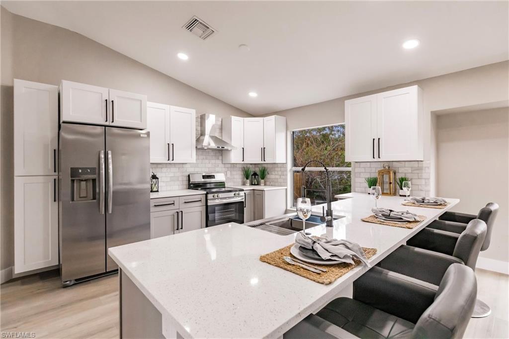 18289 Hepatica Road Fort Myers, FL 33967 - Photo 12 of 45 a kitchen with stainless steel appliances kitchen island granite countertop a refrigerator a stove a sink a dining table and chairs with wooden floor