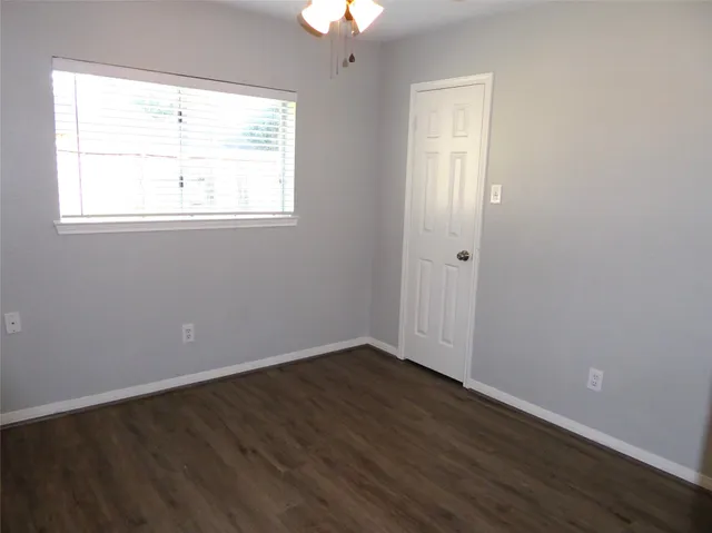 an empty room with wooden floor chandelier fan and windows