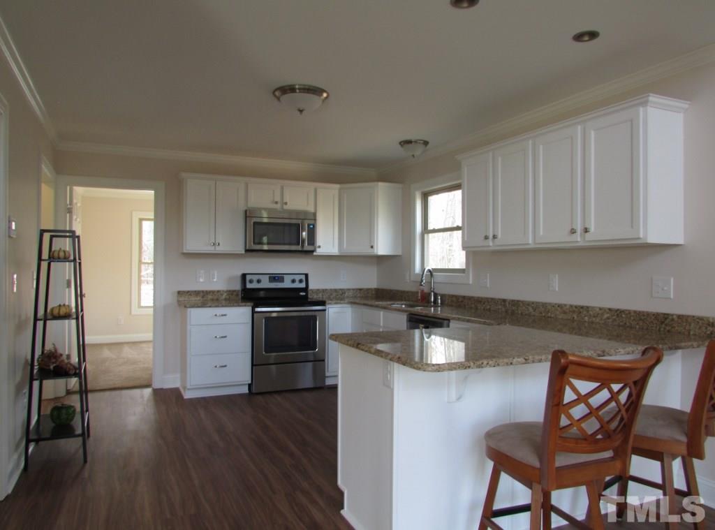 6477 Virgilina Road Roxboro, NC 27574 - Photo 5 of 20 a kitchen with granite countertop wooden floors white cabinets and stainless steel appliances