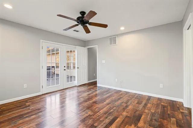a view of an empty room with wooden floor and a ceiling fan