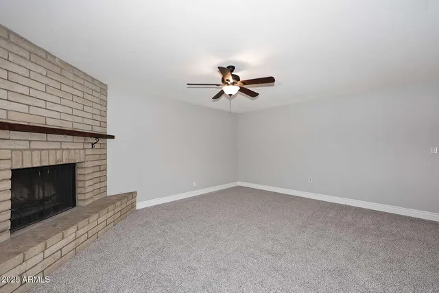 a view of an empty room with chandelier fan and fire place