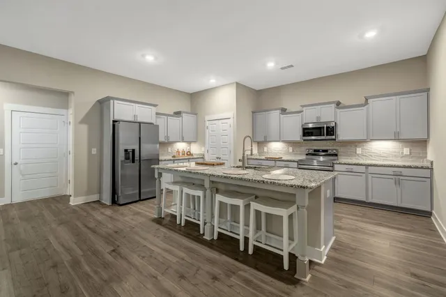 a kitchen with stainless steel appliances granite countertop a refrigerator a stove a sink and white cabinets with wooden floor