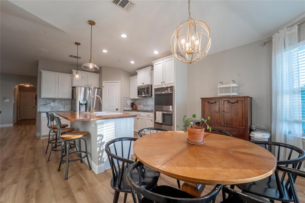 5521 Wisdom Court Waco, TX 76708 - Photo 10 of 28 Open-concept kitchen and dining area featuring wood-finish flooring, white cabinetry, stainless steel appliances, a kitchen island with a wood countertop, and decorative pendant lighting