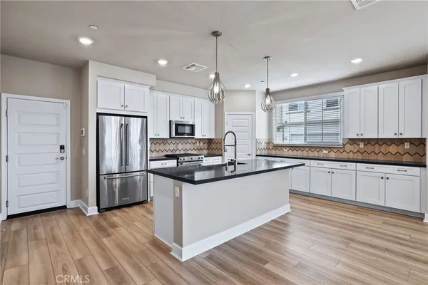 a kitchen with stainless steel appliances granite countertop a refrigerator a sink dishwasher a stove and white countertops with wooden floor
