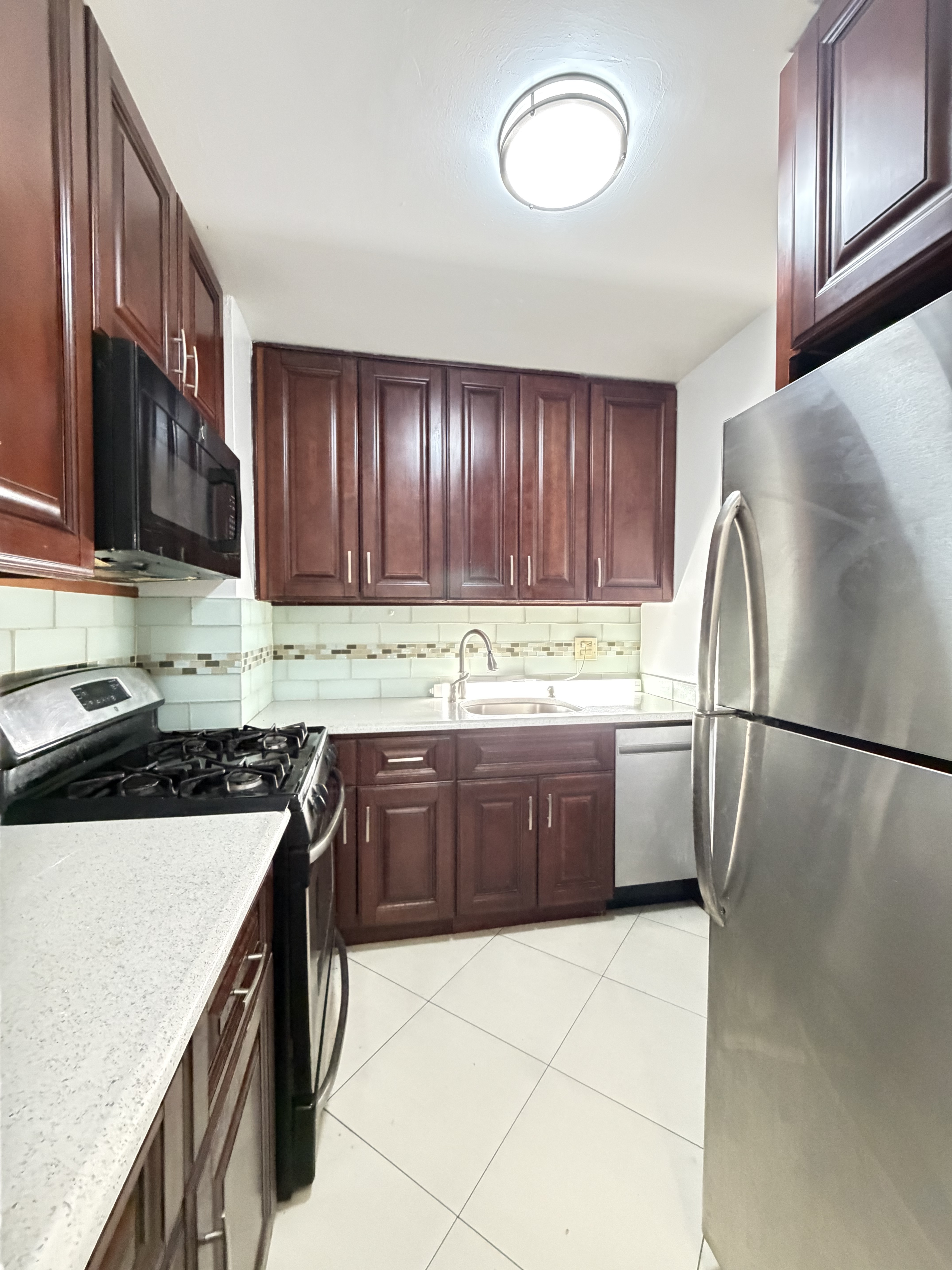 85-15 Main Street, Unit 2R Queens, NY 11435 - Photo 5 of 15 a kitchen with granite countertop a refrigerator a stove a sink and cabinets