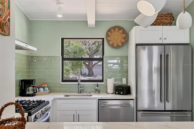 a kitchen with stainless steel appliances a stove a refrigerator a sink and a large window