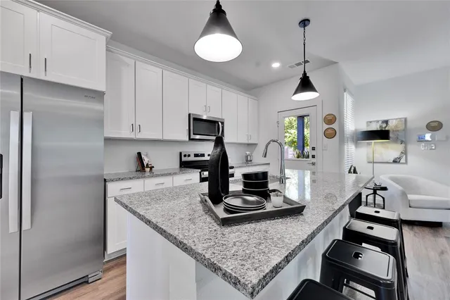a kitchen with stainless steel appliances kitchen island a white table chairs and a stove