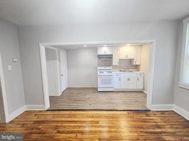 a view of kitchen and empty room with wooden floor