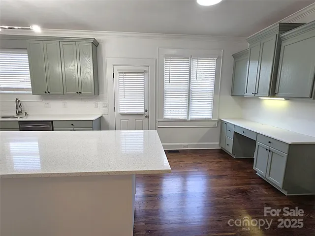 a large kitchen with granite countertop a large counter top a sink wooden floor and stainless steel appliances