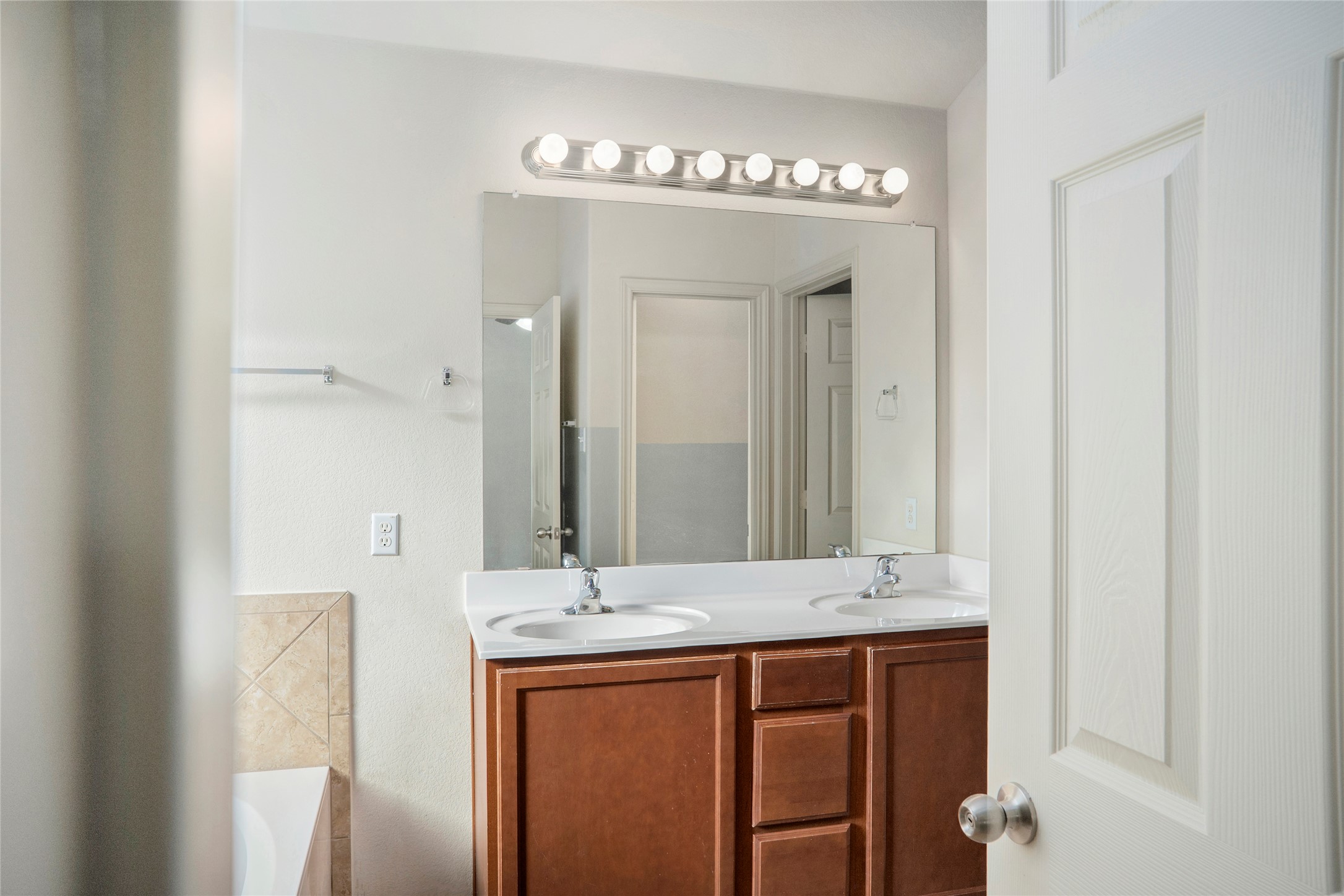 212 Foster Lane Jarrell, TX 76537 - Photo 22 of 22 Primary bath featuring a dual-sink countertop, wood-finish cabinetry, and an expansive mirror with strip lighting
