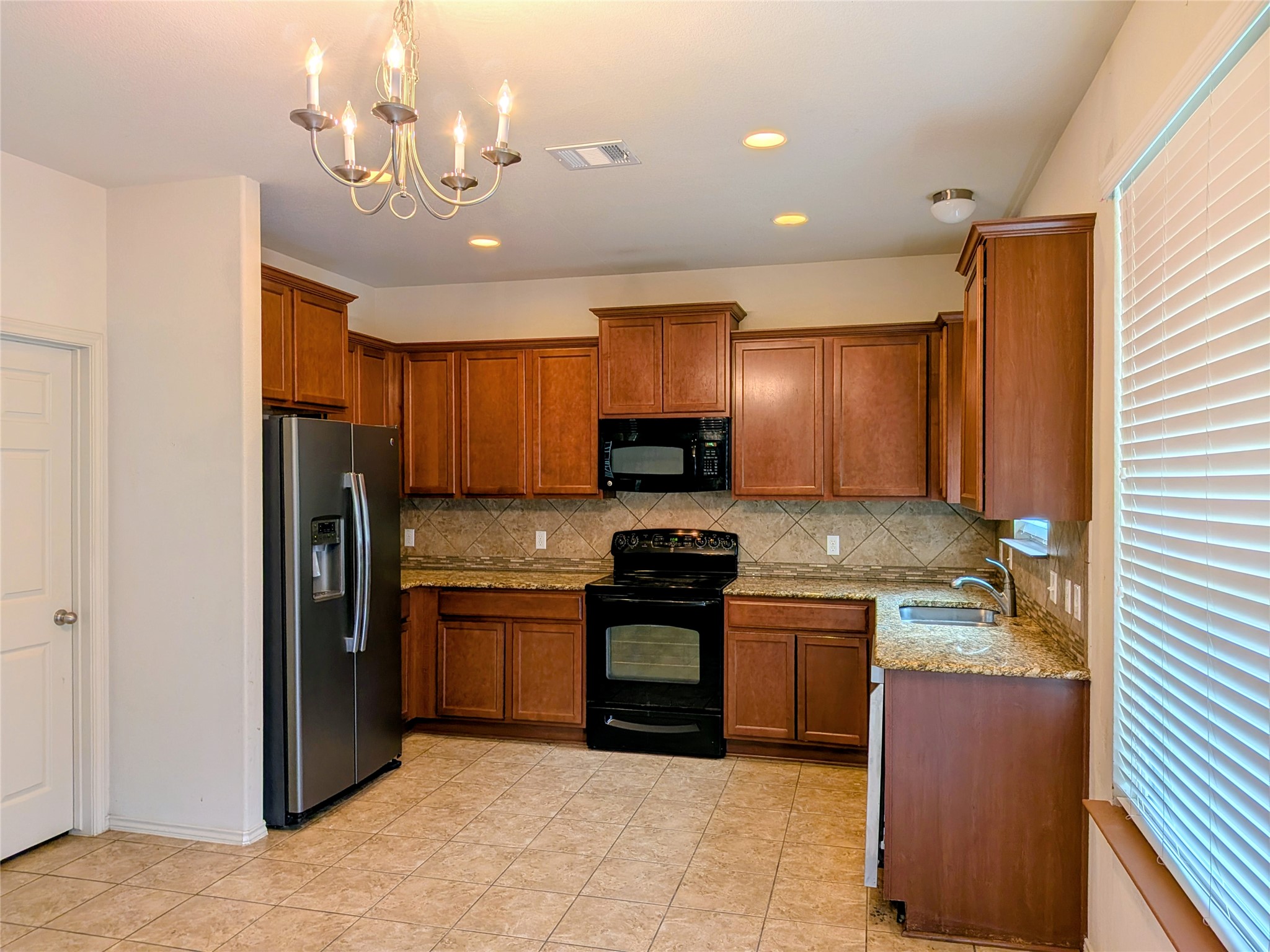 212 Foster Lane Jarrell, TX 76537 - Photo 6 of 22 Kitchen featuring wood cabinetry, granite countertops, mosaic tile backsplash, black and stainless steel appliances, and tile flooring