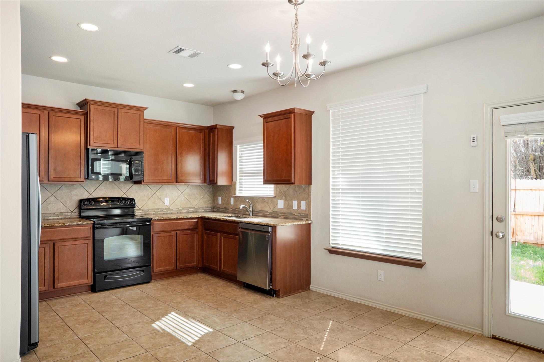 212 Foster Lane Jarrell, TX 76537 - Photo 7 of 22 Kitchen featuring wood cabinetry, stone countertops, stainless steel appliances, and a tile backsplash over looking the backyard