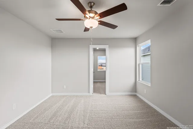 an empty room with chandelier fan and windows