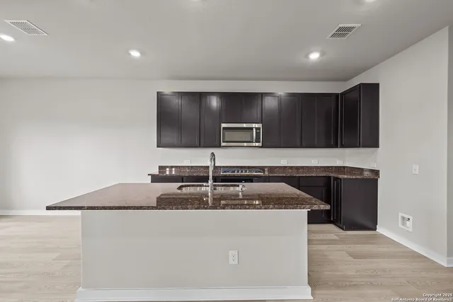 a kitchen with kitchen island granite countertop a sink and a stove top oven with wooden floor