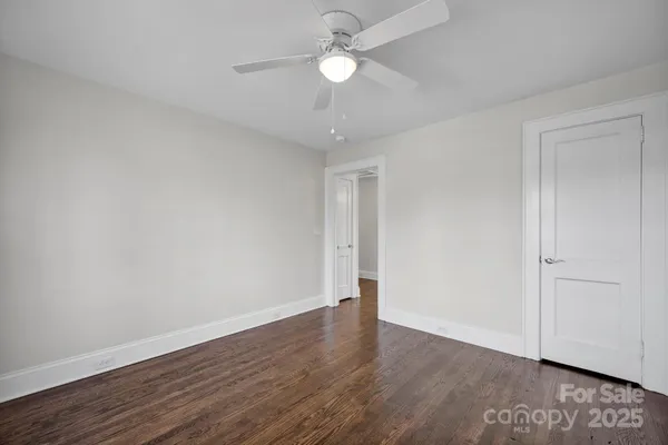 a view of an empty room with wooden floor and a ceiling fan