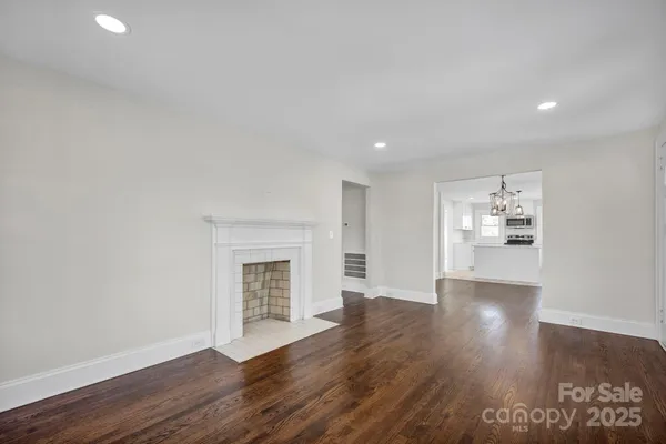 a view of an empty room with wooden floor fireplace and a window